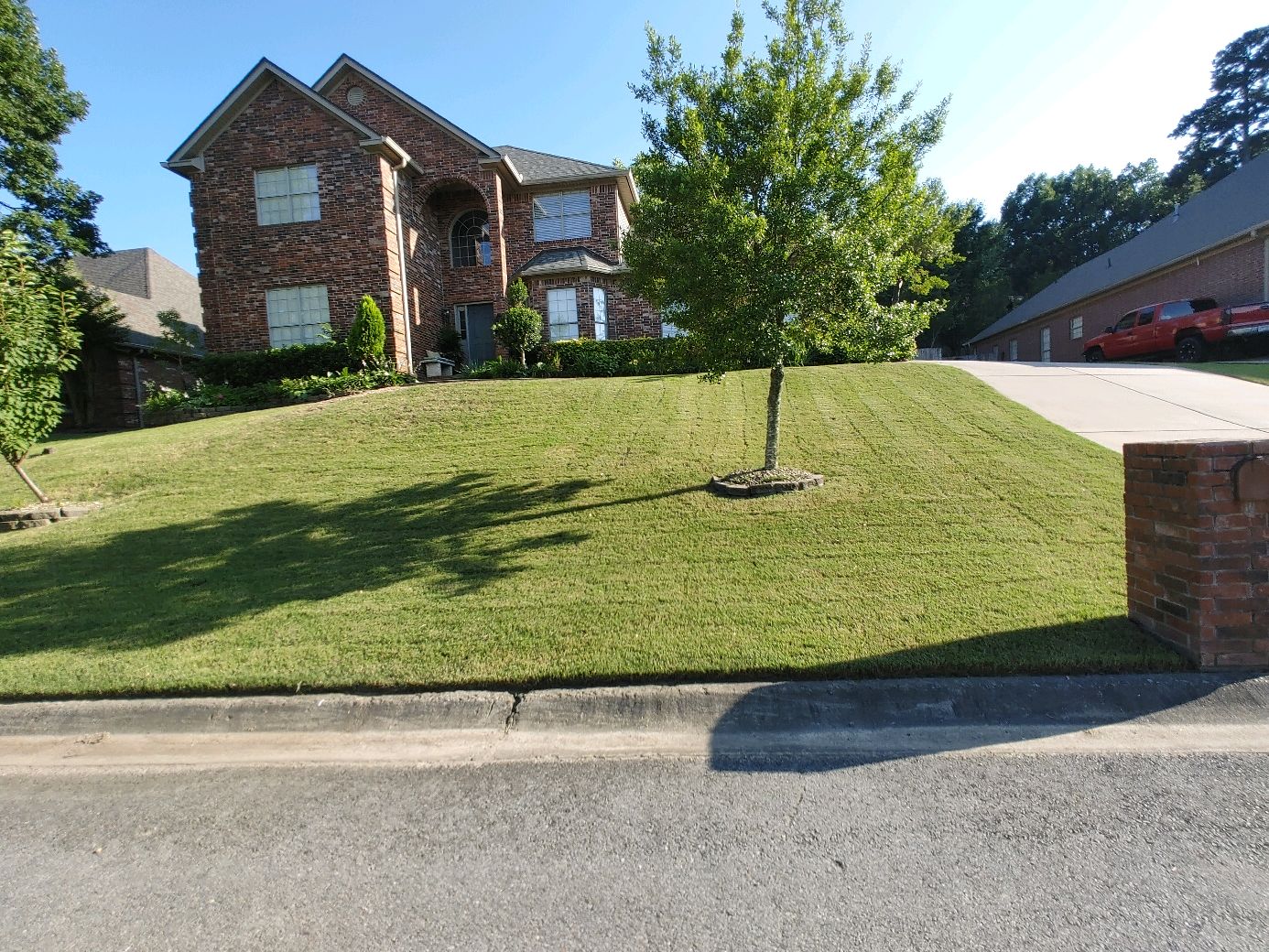 our work, an employee in a well manicured lawn in front of a two story brick house on a sunny day in the little rock metro area